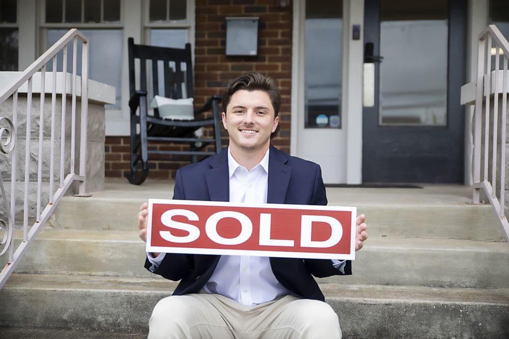 Colby Williams holding a Sold sign in front of a home